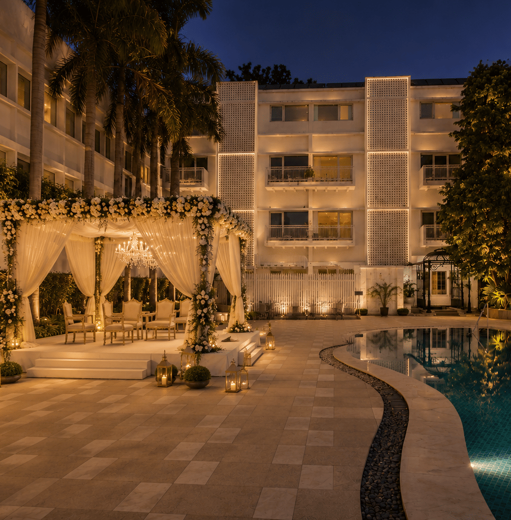 Night view of an illuminated outdoor cabana with white drapes set beside a swimming pool at a hotel courtyard - The Claridges New Delhi