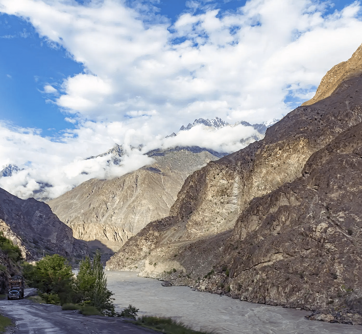 A river flowing in the foothills of a mountain with a narrow road right beside it.