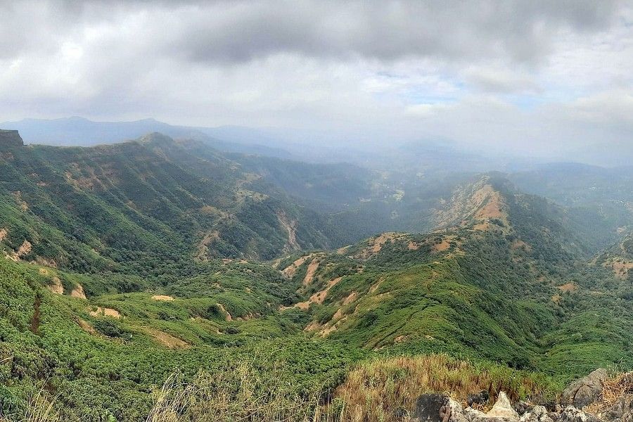 The lush landscape captured from in a birds eye view, visualised with clouds , and shot between a couple of boulders.