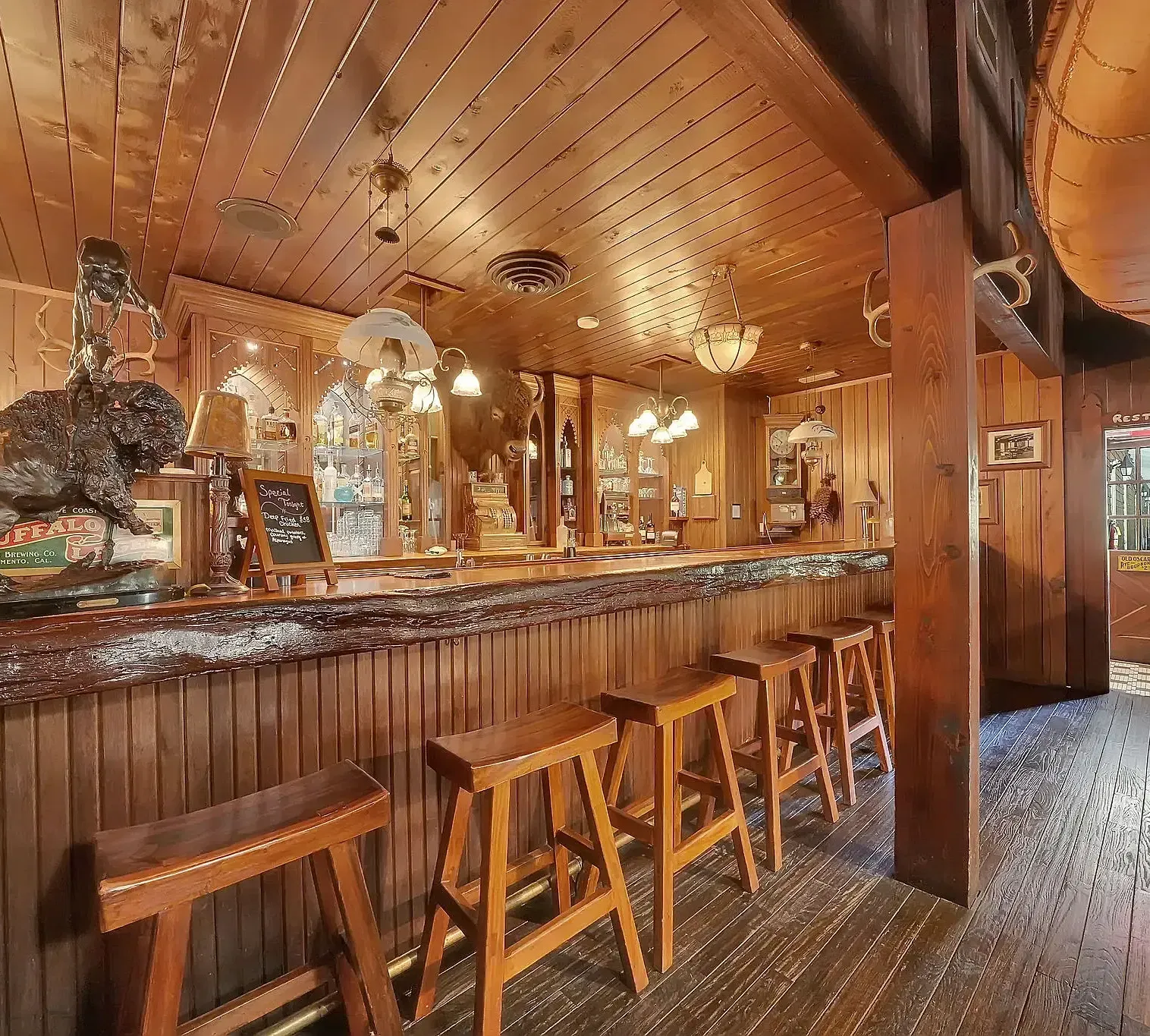 An inviting wooden bar area with high stools, warm lighting, and a polished counter lined with bottles and glassware.