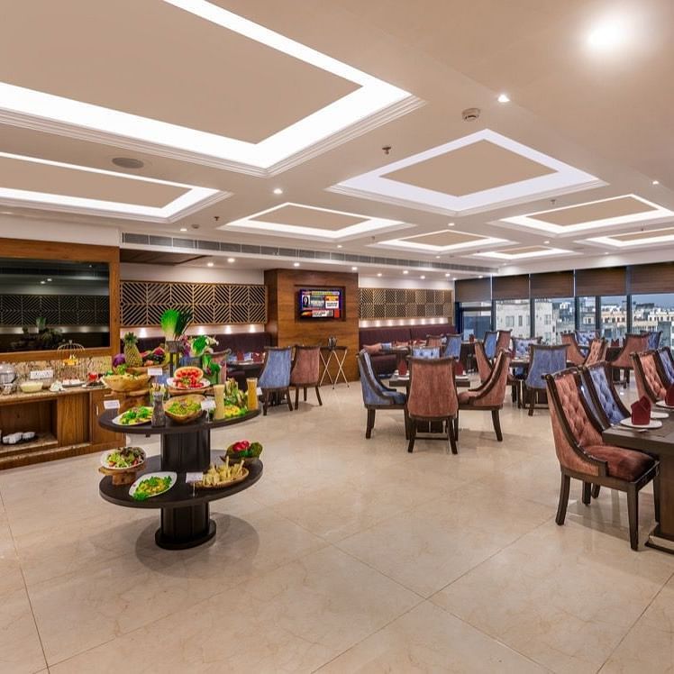 Elegant restaurant interior with multiple dining tables, cushioned chairs, and modern ceiling lighting.