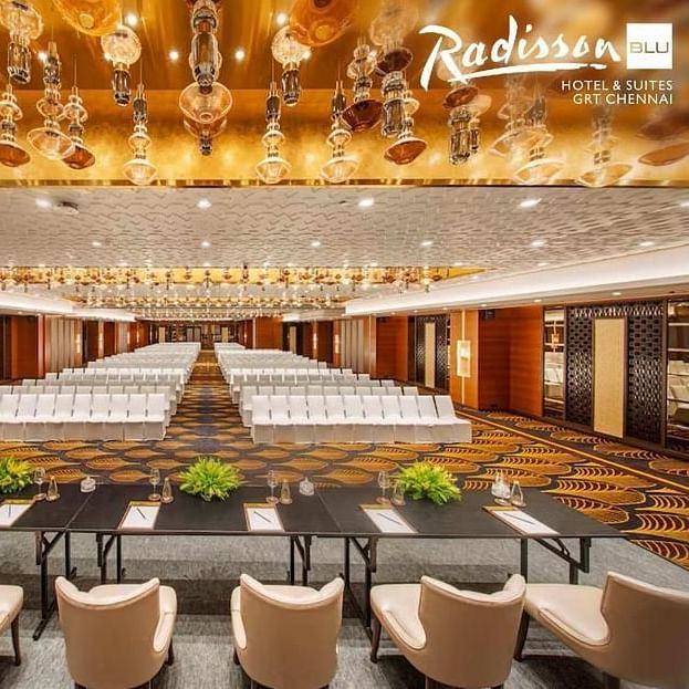 Elegant conference hall at Radisson Blu Hotel & Suites GRT Chennai with golden chandeliers and seating setup.