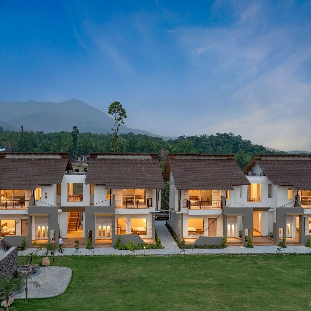 A row of luxurious villas with lit windows, surrounded by lush greenery and mountains in the distance.