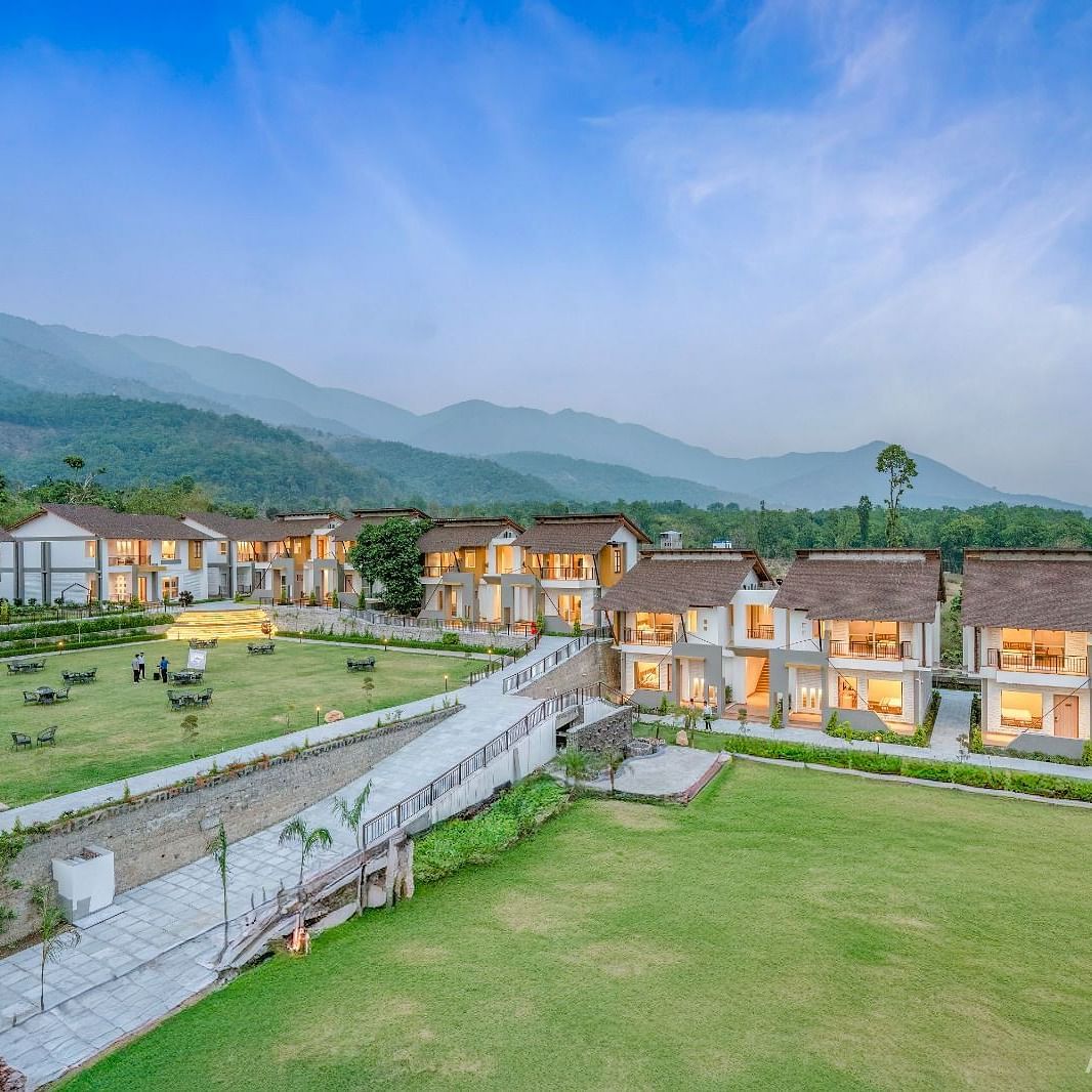 A sprawling resort complex with multiple buildings, a central lawn, and a scenic mountain backdrop.