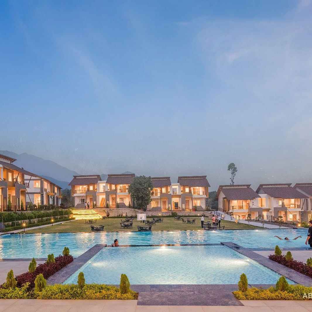 A large resort with multiple buildings surrounding a swimming pool, under a twilight sky.