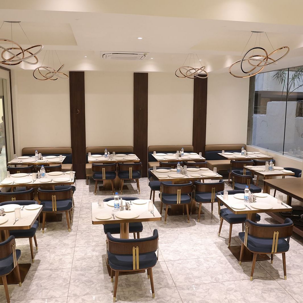 A brightly lit dining area at Lords Eco inn Jamnagar Maheshwari Nagar with multiple tables chairs and stylish lighting.