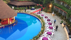 Uday Suites shows a pool, thatched-roof structure, and outdoor dining setup along a walkway
