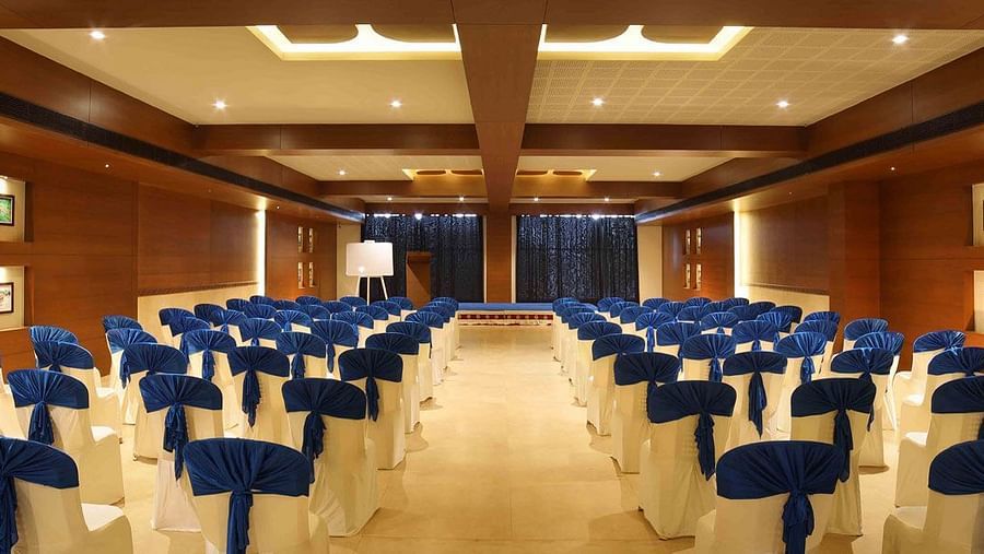 House Boat Hall at Uday Backwater Resort featuring chairs arranged in a way that they are facing the podium in front of them with a blue colour backdrop under warm lighting