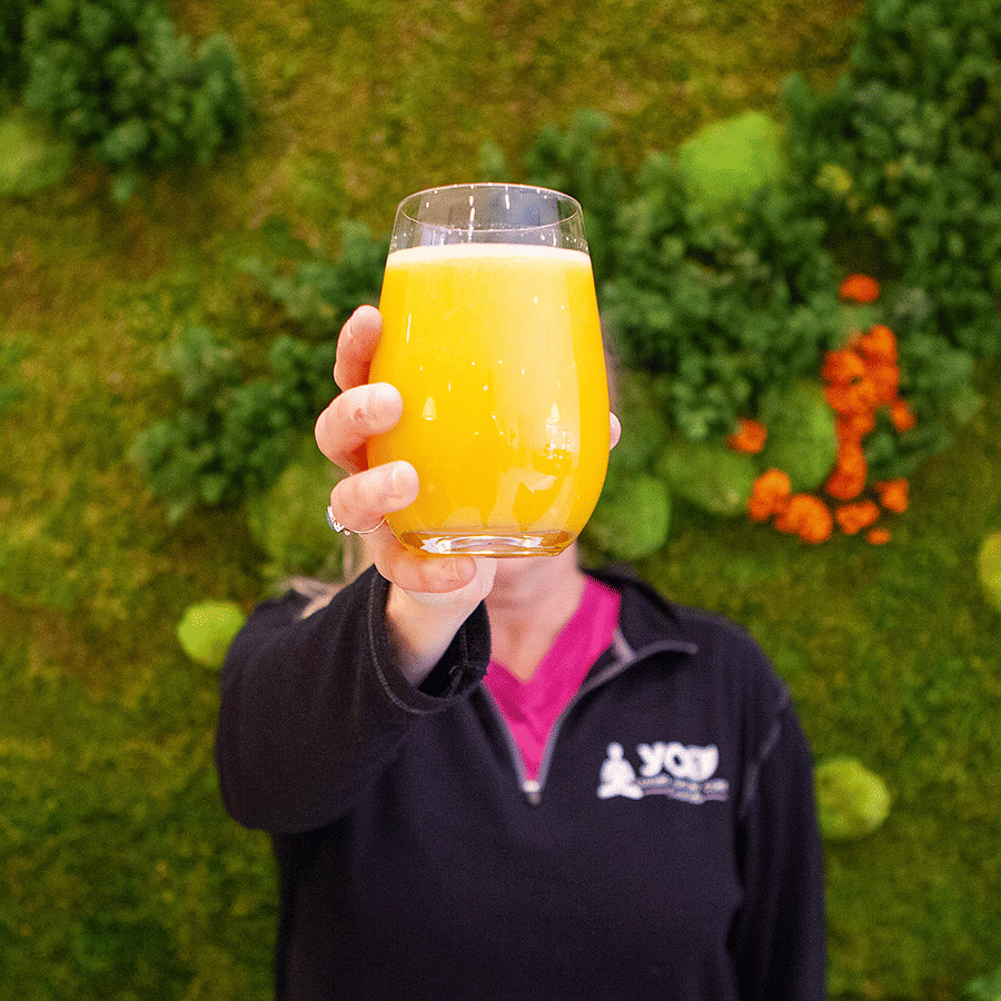 Refreshing orange juice held up against a green wall at YO1 Longevity and Health Resorts, Catskills
