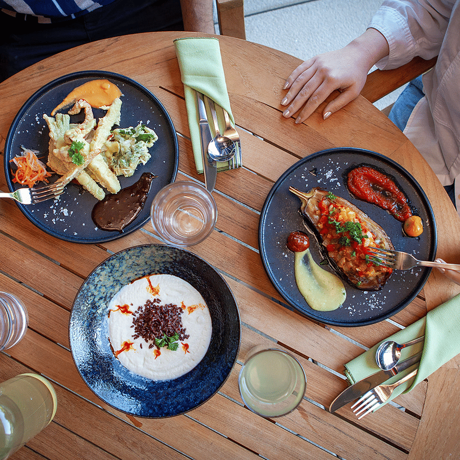 A round dining table with three platters of food on it and a couple of people eating at YO1