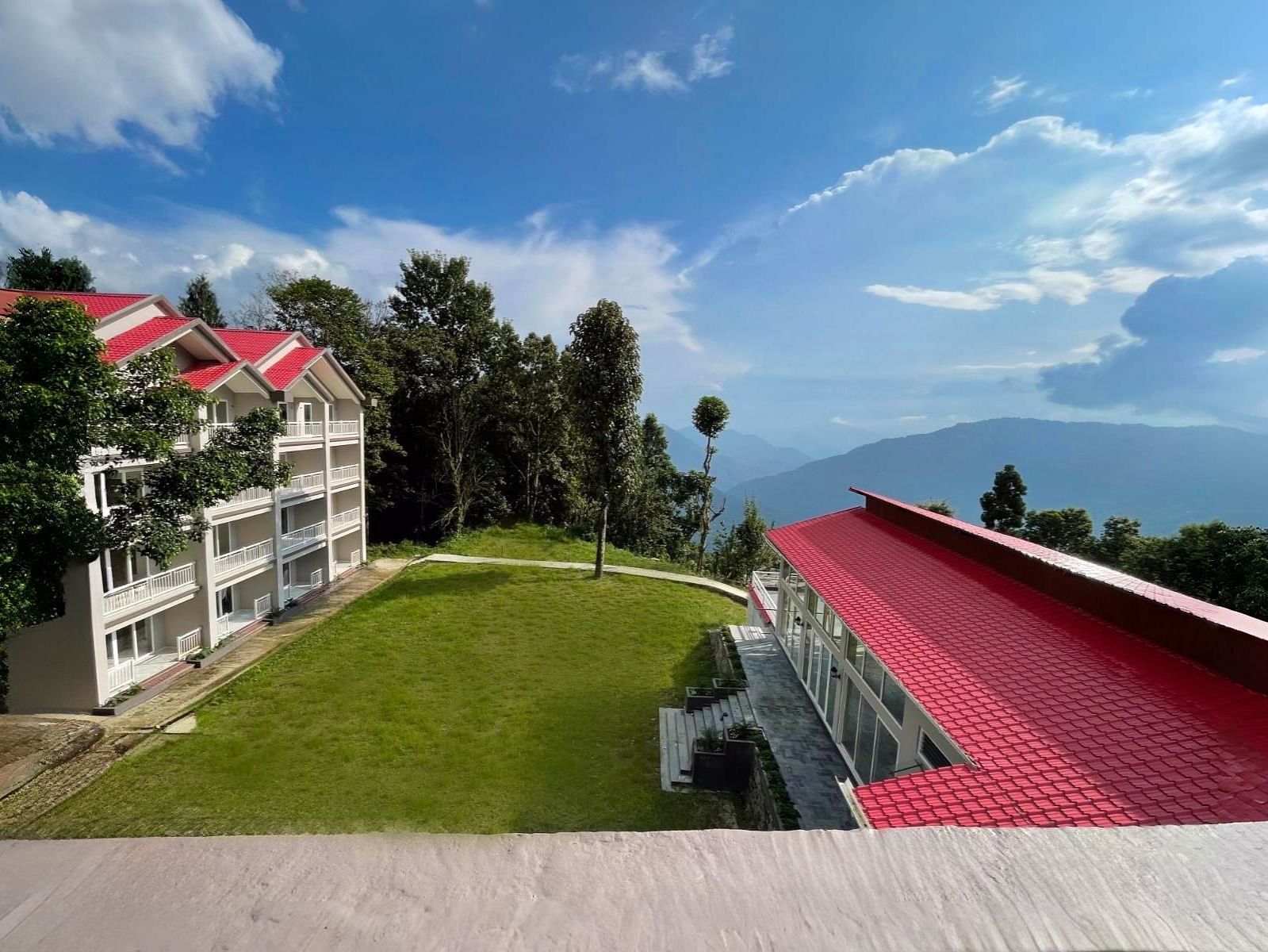 A scenic view of the buildings and landscape at Yashshree Resorts & Spa, Kalimpong, showcasing a distinctive red-roofed structure amidst the greenery and rolling hills.