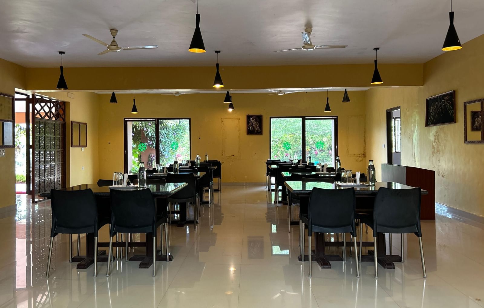 Restaurant interior with tables, chairs, indoor tree section, and yellow walls at Paradise Wild Hills Resort, Kollur.