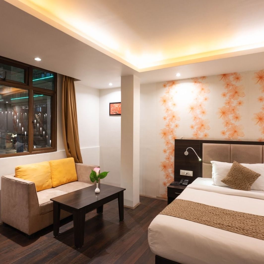 Deluxe Room at Avianna Hungry Jack, Gangtok featuring a plush bed next to a sitting space with a two-seater sofa and a coffee table by the window under warm lighting