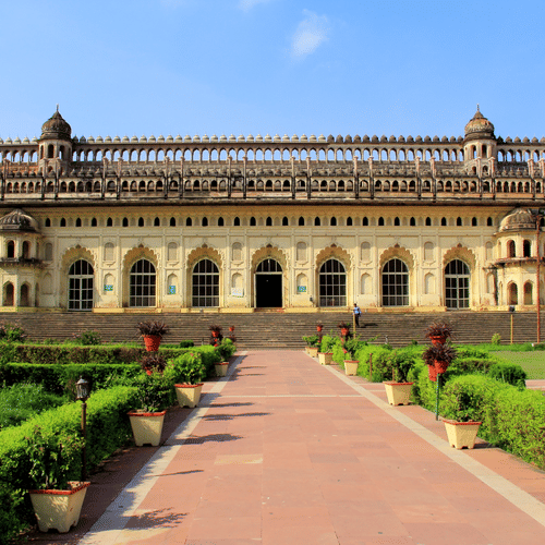 A wide-angle view of a large, beautiful historical palace with a long, stone walkway leading up to it through a green lawn.