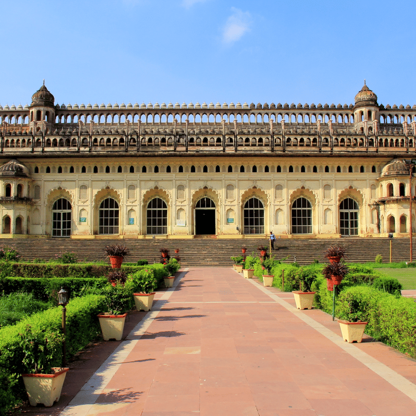 A wide-angle view of a large, beautiful historical palace with a long, stone walkway leading up to it through a green lawn.