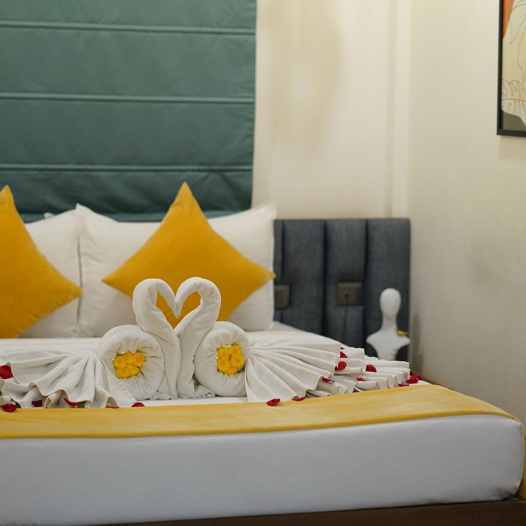 A room with a neatly made double bed adorned with yellow and towels shaped into swans, scattered with rose petals for a welcoming touch at Kyzen Smart Stays.