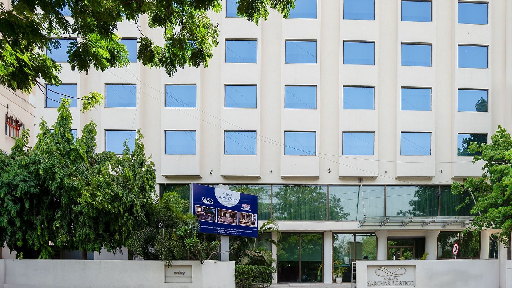  A facade image of the Marasa Sarovar Portico, Rajkot with trees around.