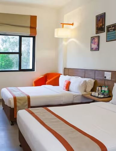 View of a hotel room featuring two comfortable beds, wall art, and a large window with natural light - Max Hotel Prayagraj.