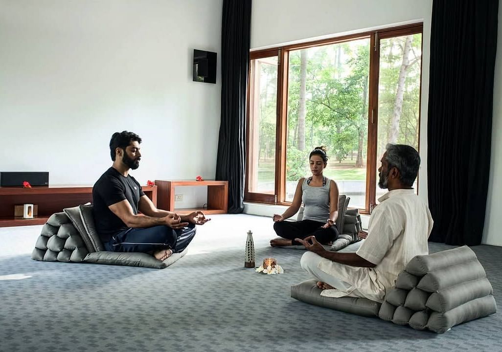 A couple participating in Trataka meditation along with a yoga teacher in a closed yoga space - Shreyas Retreat