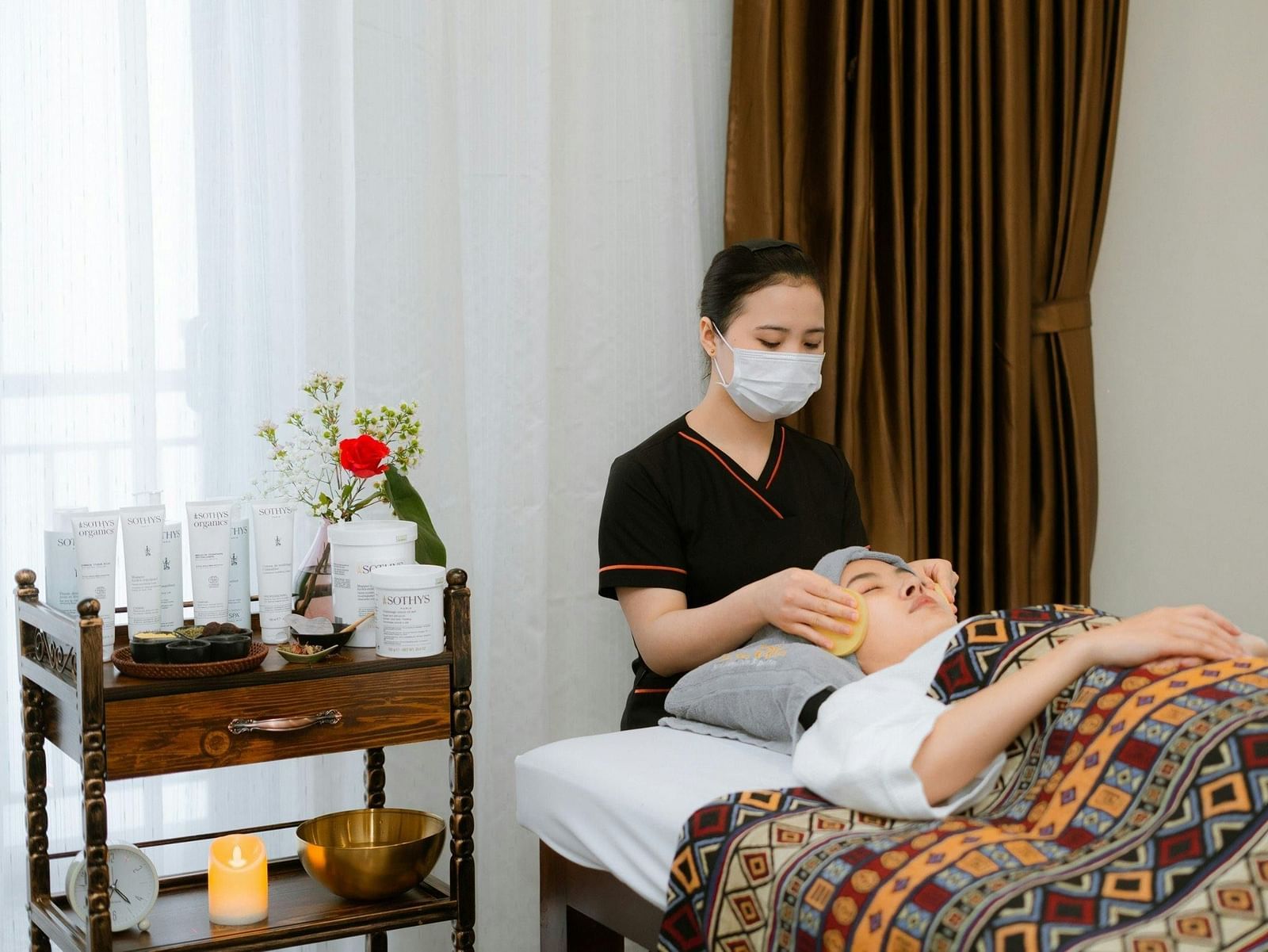 At the Best Family Hotel in Udaipur, a woman stands behind another, giving her a spa massage, with a table nearby holding spa equipment