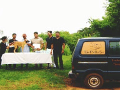 group of people standing besides a van in front of a table talking to each other