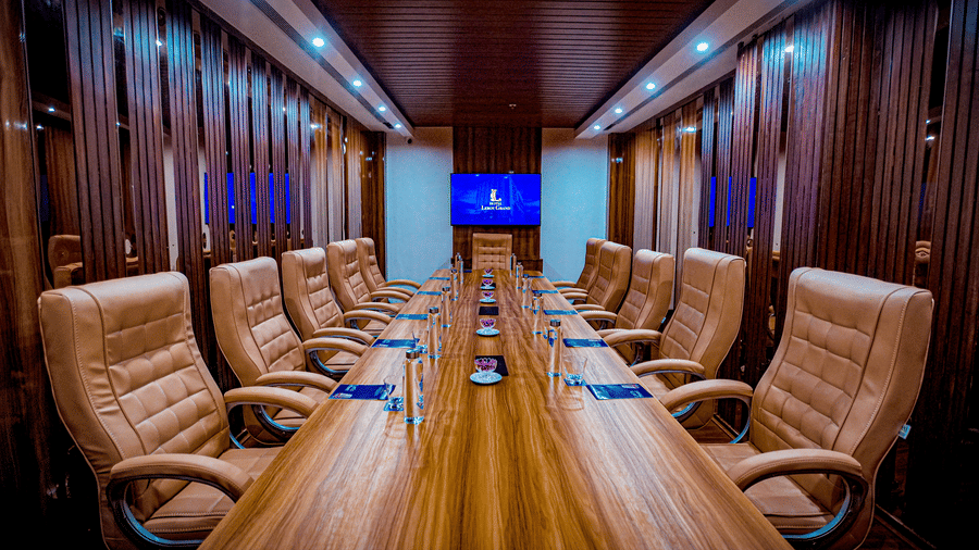 Front view of the conference table in a boardroom at Leroy Grand, Yeshwanthpur, surrounded by beige-coloured tufted leather chairs and a wall-mounted television at the far end of the room.