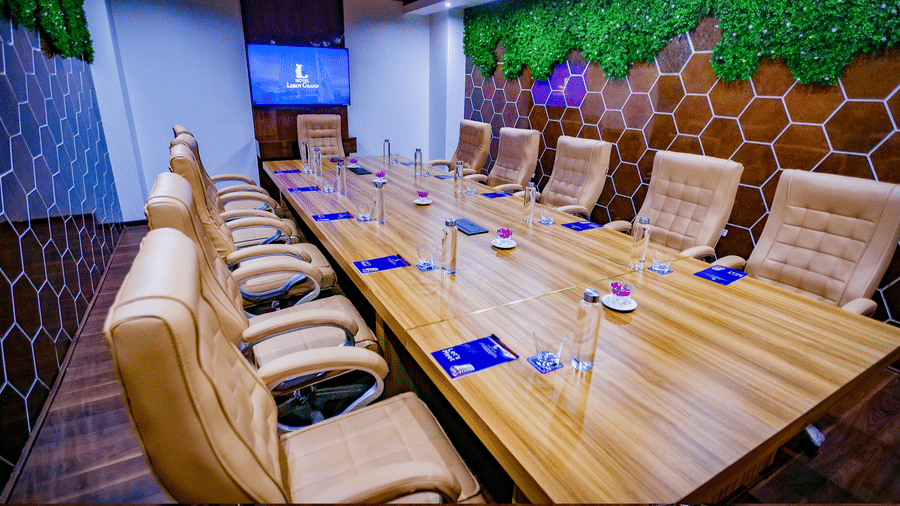 An overhead shot of the boardroom at Leroy Grand, Yeshwanthpur, with basic stationary items placed in front of each seat on the wooden table along with a glass of water.