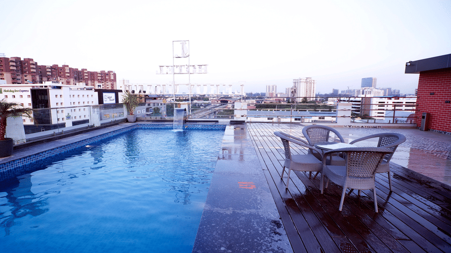 A wide-angle shot of the Kensho poolside rooftop pub featuring a dining table by the pool on the wooden deck at Leroy Grand, Yeshwanthpur.