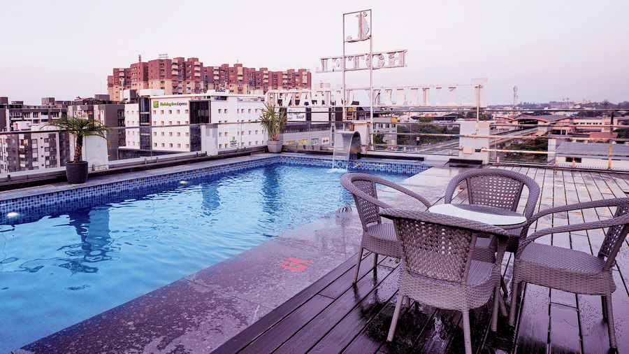 An overhead shot of a dining table surrounded by 4 chairs by the pool overlooking the neon sign board of Leroy Grand, Yeshwanthpur.