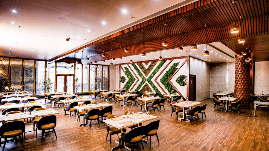 A wide angle shot of the Punarvasu restaurant with dining tables equidistantly arranged to each other, with the glass entrance doors at the far end of the restaurant at Leroy Grand, Yeshwanthpur.