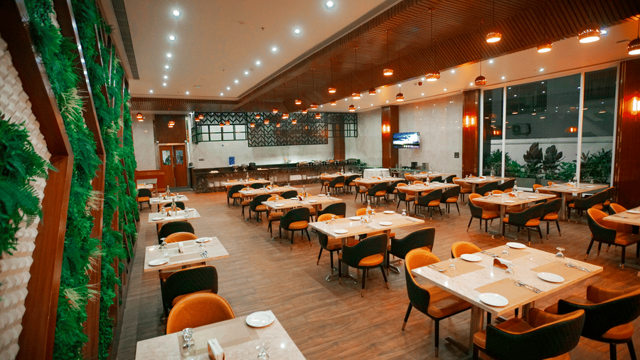 Punarvasu restaurant during the late evening hours at Leroy Grand, Yeshwanthpur, featuring several dining tables set with cutlery and glassware.