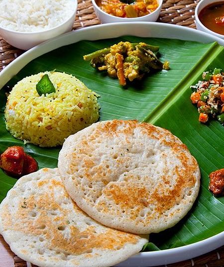 A plate of food with rice, vegetables, and flatbread on a green leaf-shaped plate - Shreyas Retreat