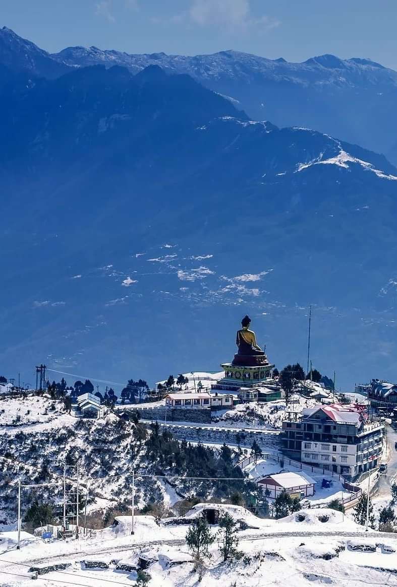 Snow-covered town with a monastery perched on a hill, overlooking misty mountains in the distance.