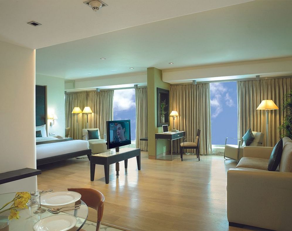 Shot of the expansive suite at our hotel featuring a separate living area, sofa, side lamp, a television, and a king size bed. | Mirage Hotel