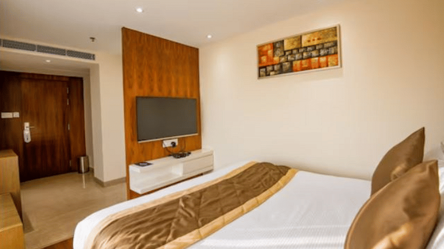 A neatly arranged hotel room with a large bed, a wall-mounted TV, and a colourful painting above the bed at Yashshree The Imperial Inn, Siliguri