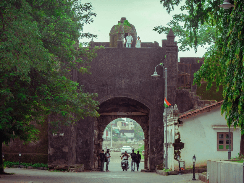 Historic stone gateway of Moti Daman Fort surrounded by trees and visitors.