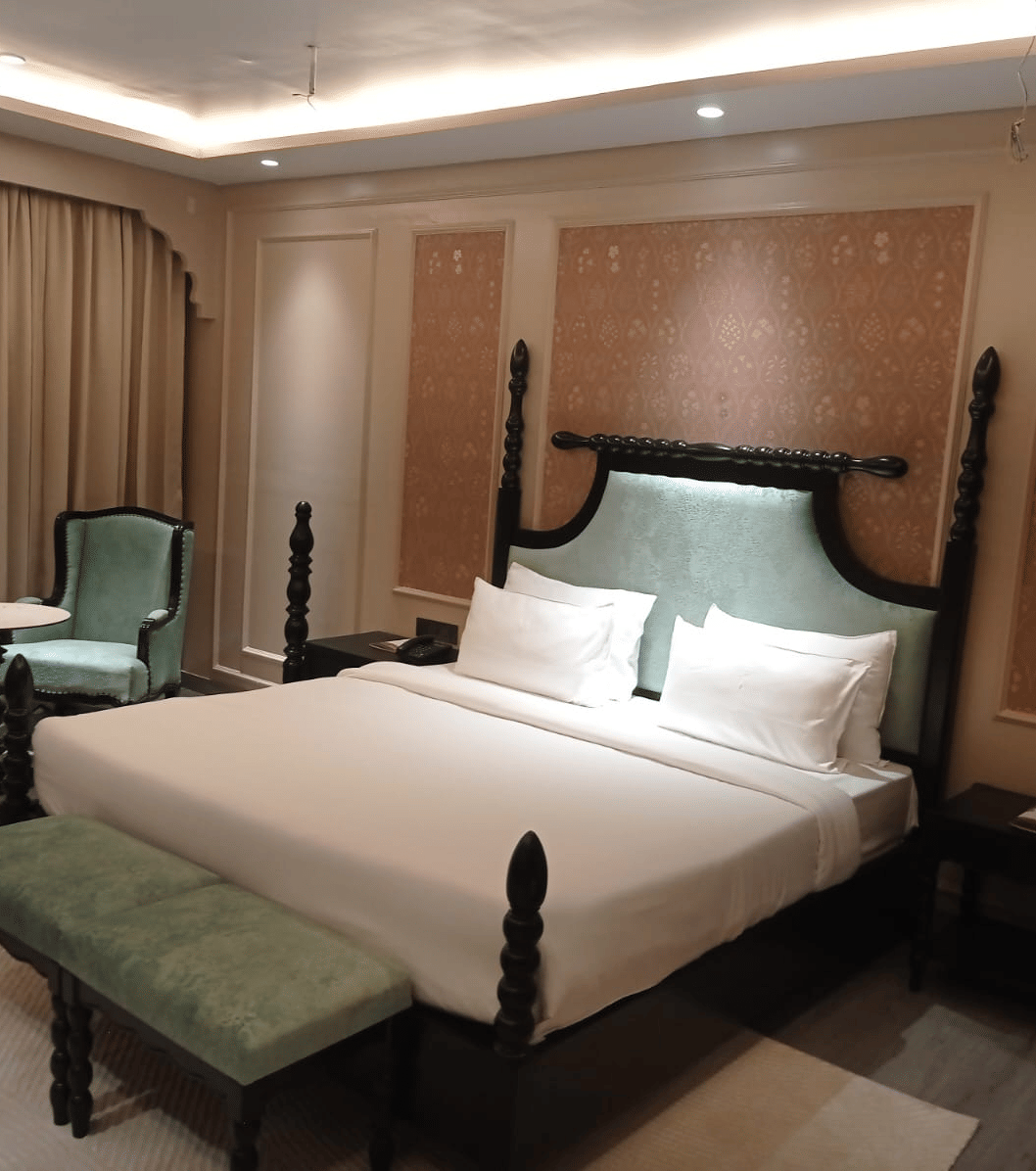 Bedroom with king size bed, side tables, chairs and window curtain at Beelwa Palace, Jaipur