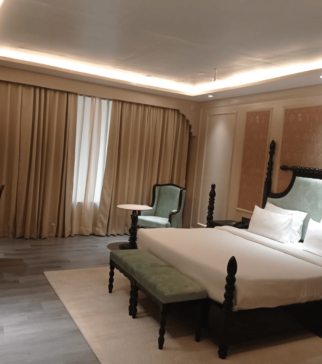 Bedroom with double bed, chairs, desk and curtains along the wall at Beelwa Palace, Jaipur