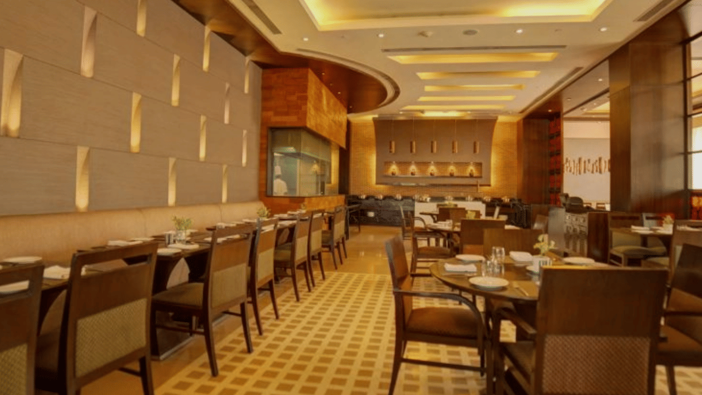 Restaurant interior at Goldfinch Bengaluru showing rows of dining tables, upholstered chairs, and wood panel walls.