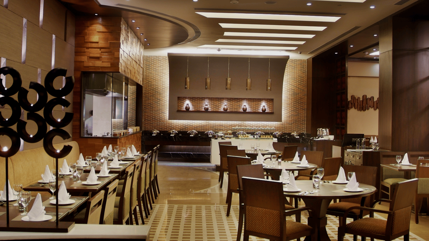 Dining area at Goldfinch Bengaluru featuring wooden tables, dark chairs, partition screens, and overhead lighting.