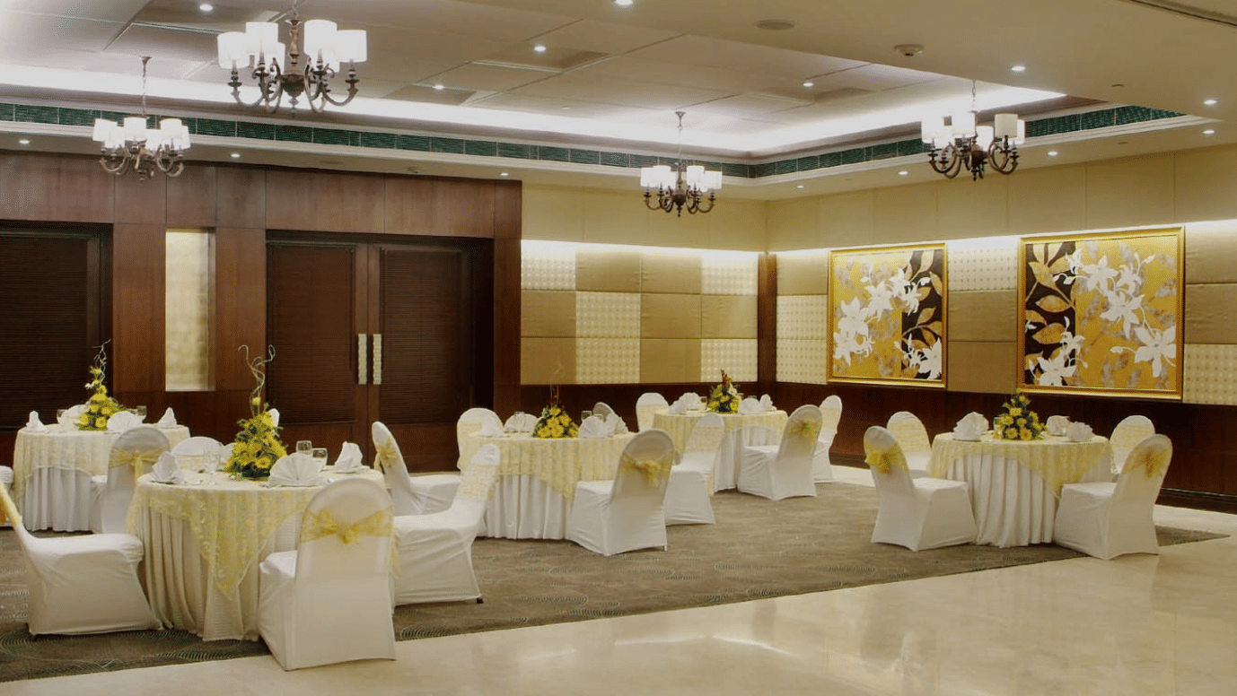 An event room at Goldfinch Bengaluru with round banquet tables, white chair covers, and dark wood wall panels.