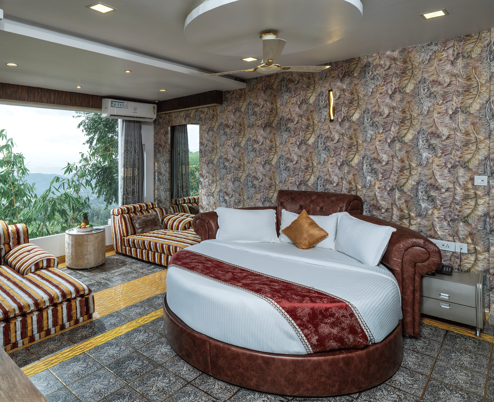 A bedroom in Family Jacuzzi Room featuring a round bed, a seating area beside large glass windows, and patterned walls.