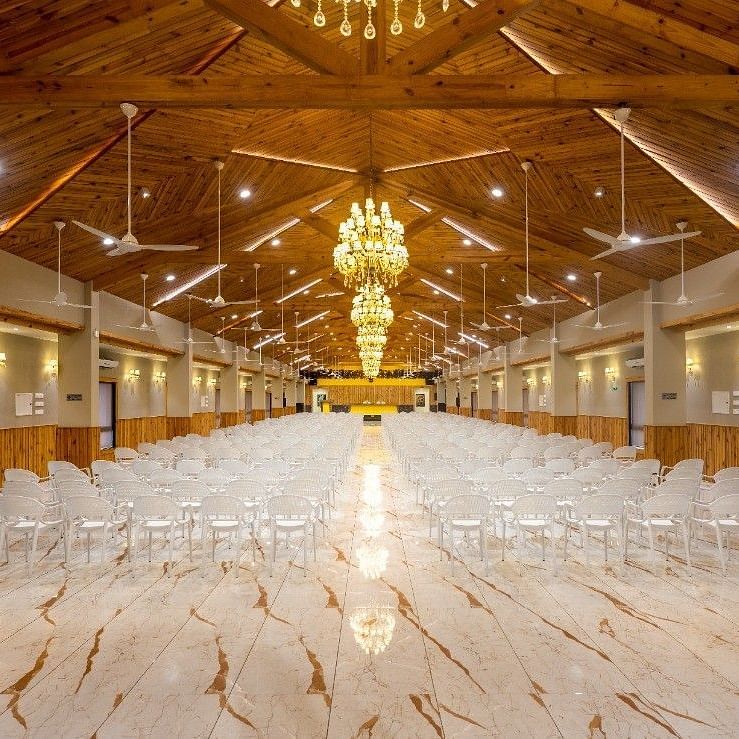 A wide view of a large banquet hall with numerous tables and chairs set under ornate lighting at Angel Lords Eco Inn Amreli.