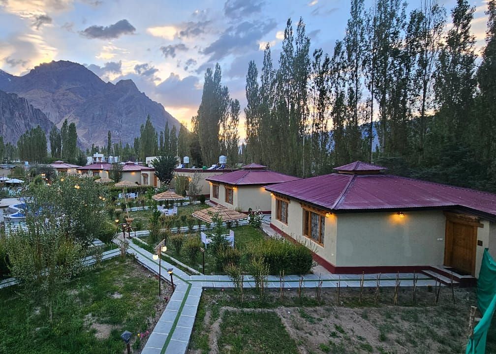 Panoramic view of White Sand Resort, Ladakh with cabins, trees, mountains, and a pathway.