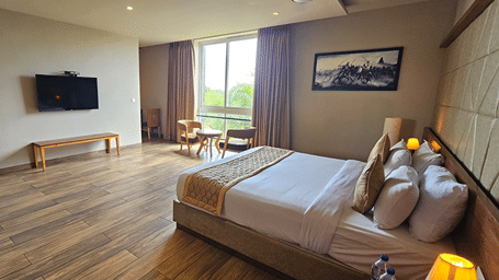 Bed with white sheets and a wall-mounted television at Cholaa Dynasty, Kumbakonam.