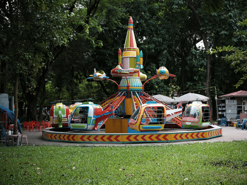 A ride at an amusement park in the centre, with a manicured lawn area in the foreground and trees in the background