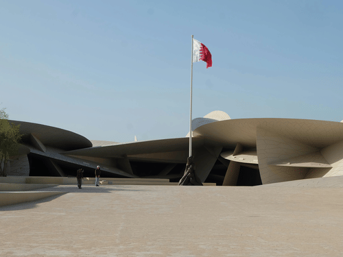 The National Museum of Qatar featuring its iconic interlocking disc architecture and the Qatari flag on a tall pole.