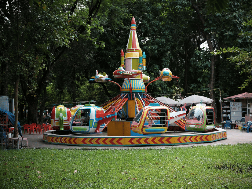 A ride at an amusement park in the centre, with a manicured lawn area in the foreground and trees in the background