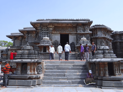 A view of the Hoysaleswara Temple with steps leading to the entrance and people walking near it.