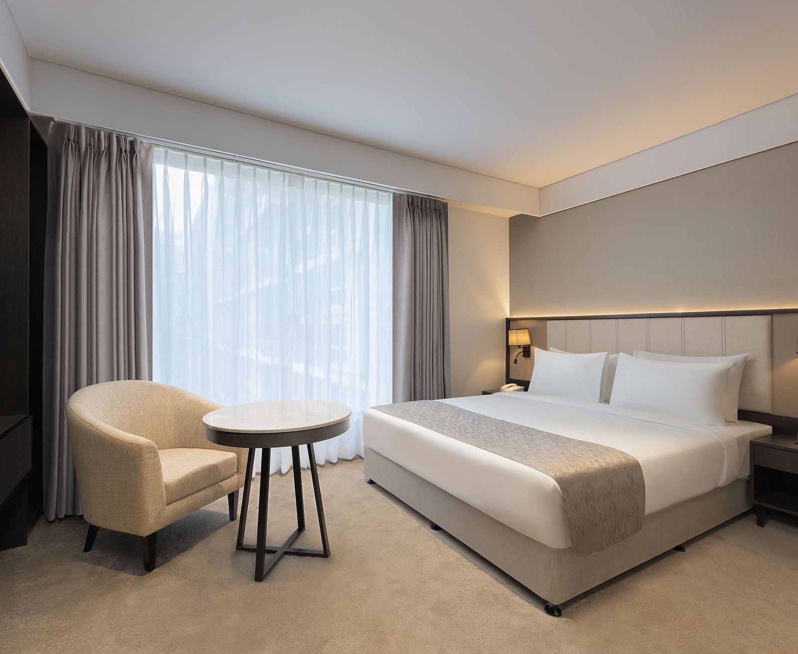 Deluxe King Room with a king size bed and a comfortable chair beside a large window at Essentia Premiere, Pune. 